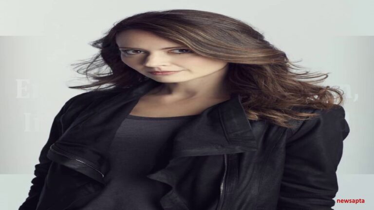 Woman with long brown hair wearing a black jacket, standing against a neutral background.