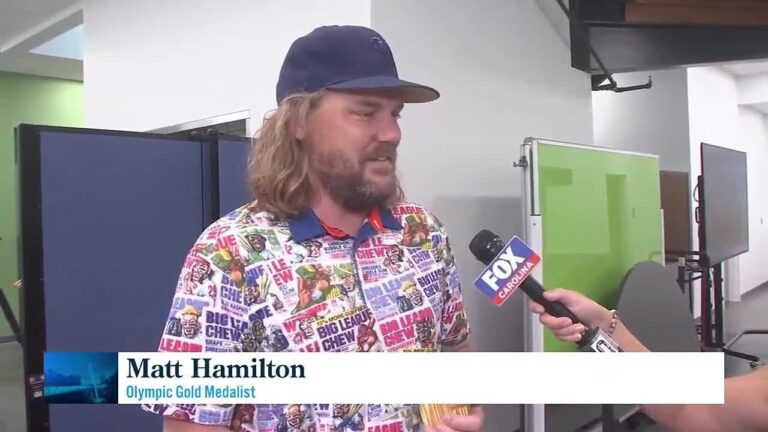 A man with a beard and long hair, wearing a colorful shirt and a cap, is being interviewed by someone holding a Fox microphone.