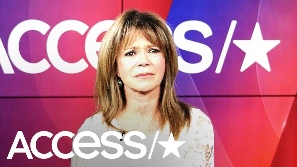 A person with long brown hair stands in front of a colorful background with the word "Access" and star logo partially visible.