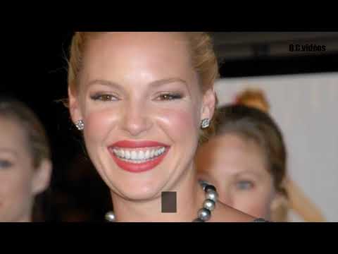 A woman with blonde hair smiles broadly, wearing pearl earrings and a necklace.