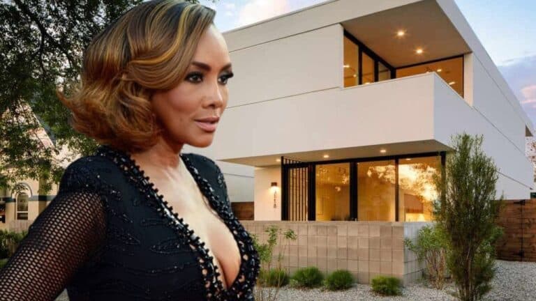 A person in a black outfit stands in front of a modern two-story house with large windows and a minimalist design.