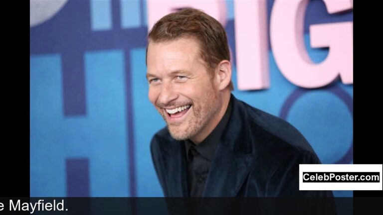 A person in a dark jacket smiles broadly at an event with blue and pink decor.