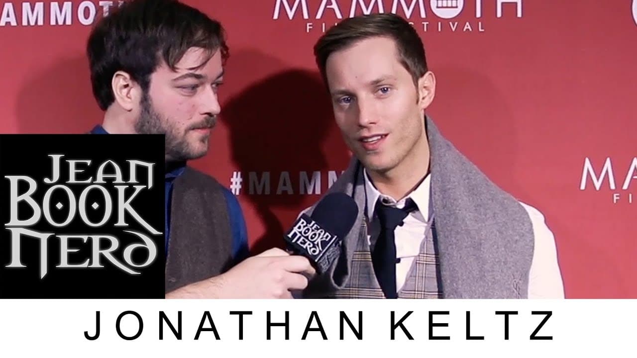 Two men are at the Mammoth Film Festival. One holds a Jean Book Nerd microphone towards the other, who is wearing a tie and vest. A banner is in the background.