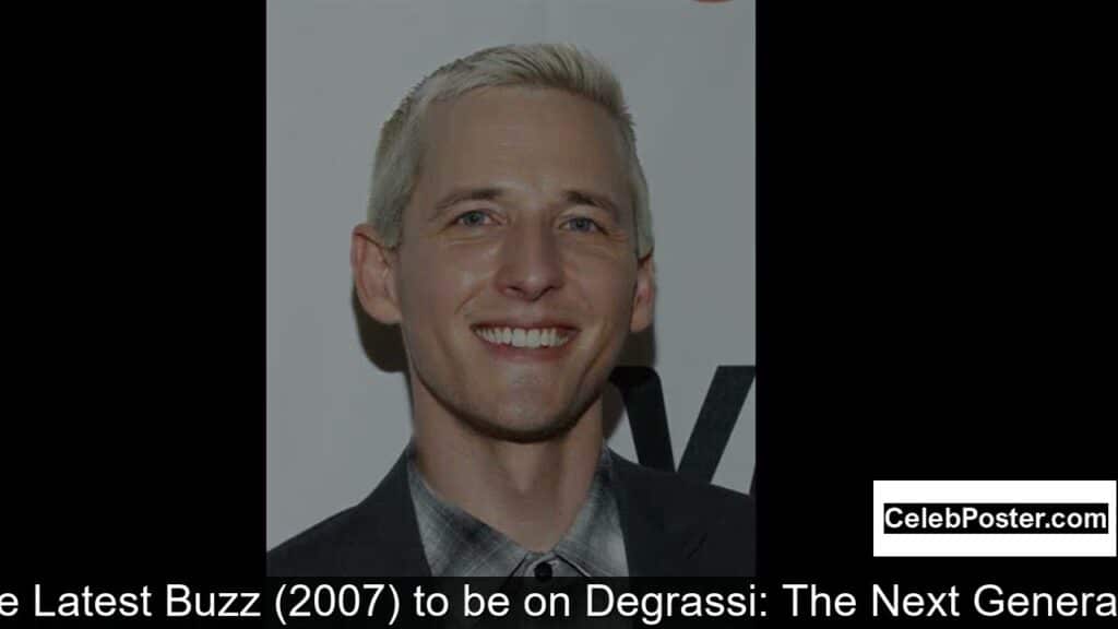 A person with short blond hair wearing a suit, smiling in front of a plain background.