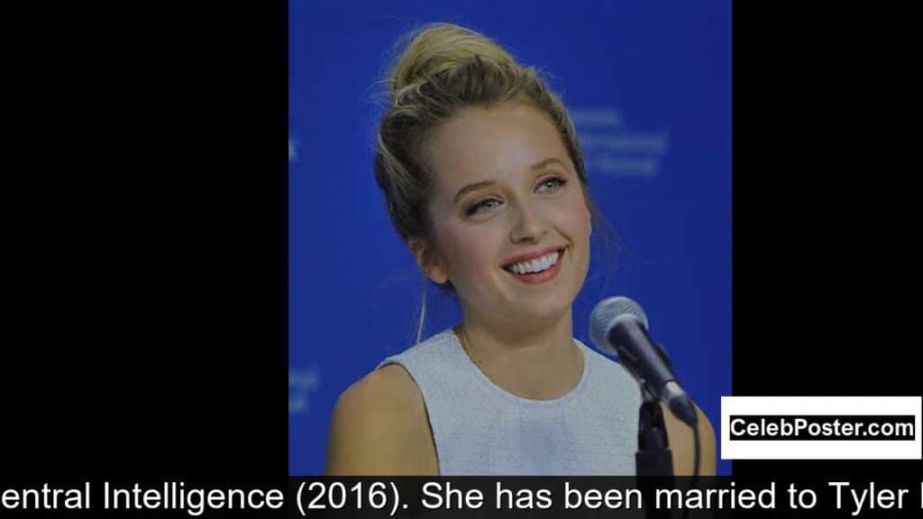 A person smiling at a speaking event with a blue background and microphone.