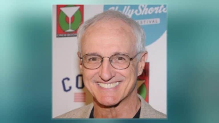 A smiling man with glasses and gray hair is standing in front of a colorful background with various logos.