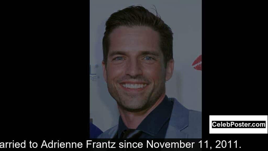 Man in a suit smiling at the camera at an event with a backdrop. CelebPoster.com logo in the corner.