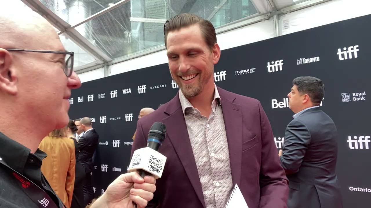 A man in a maroon jacket is interviewed by another man holding a microphone at a TIFF event.