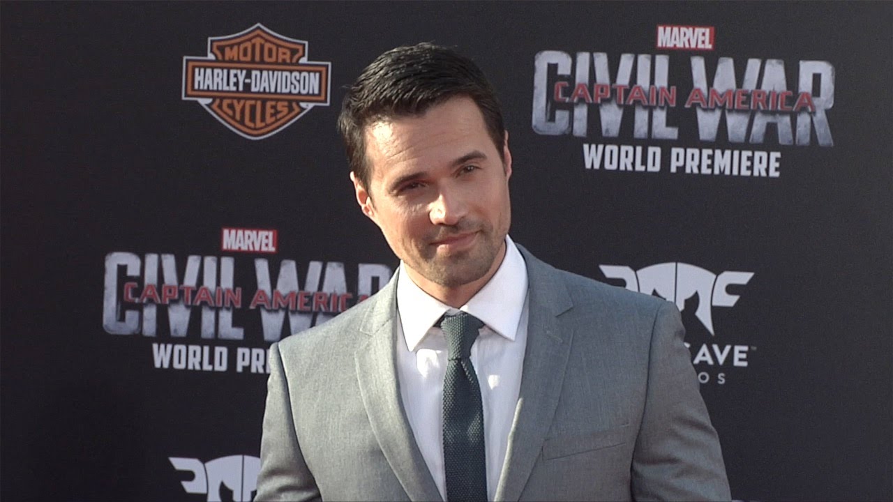 Man in a gray suit and tie standing on the red carpet at the "Captain America: Civil War" world premiere, with logos in the background.